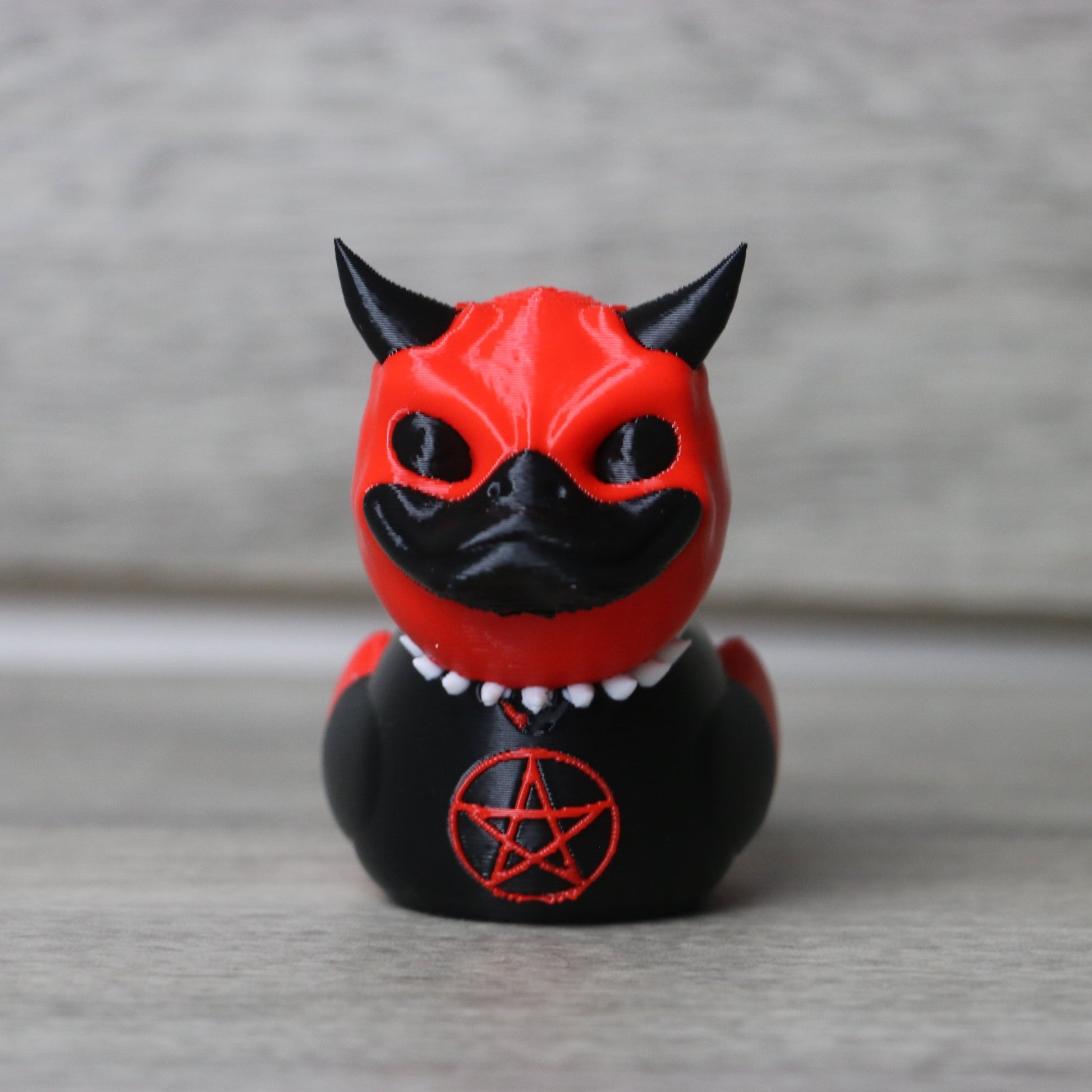 Black and red figurine with horns and a pentagram symbol on a gray background
