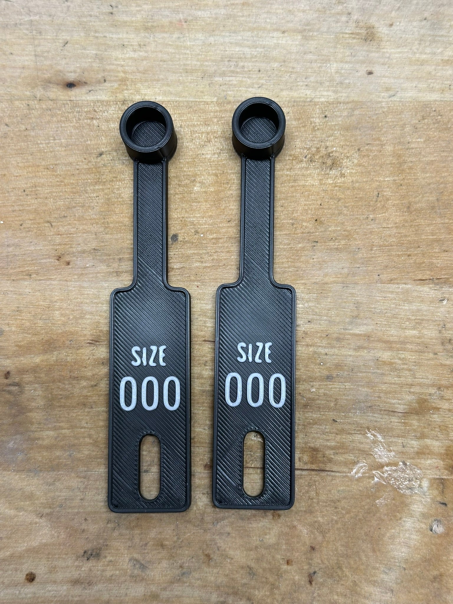 Two black size tags labeled 'SIZE 000' on a wooden surface.